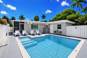 Ein Schwimmbecken mit Liegestühlen, einer überdachten Terrasse und einem weißen Zaun.