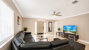 Ein Wohnzimmer mit Ecksofa, Couchtisch, Fernseher und Deckenventilator.