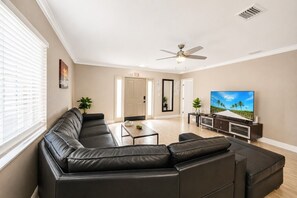 Ein Wohnzimmer mit Ecksofa, Couchtisch, Fernseher und Deckenventilator.
