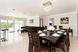 A dining area with a long table set for six, surrounded by chairs, with a chandelier above and a painting on the wall. - First-Class Villa in Hollywood Lakes Heated Pool (Hollywood)