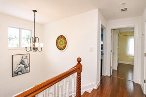 Un escalier avec une rampe en bois menant à un palier agrémenté d’un lustre et d’œuvres d’art murales.