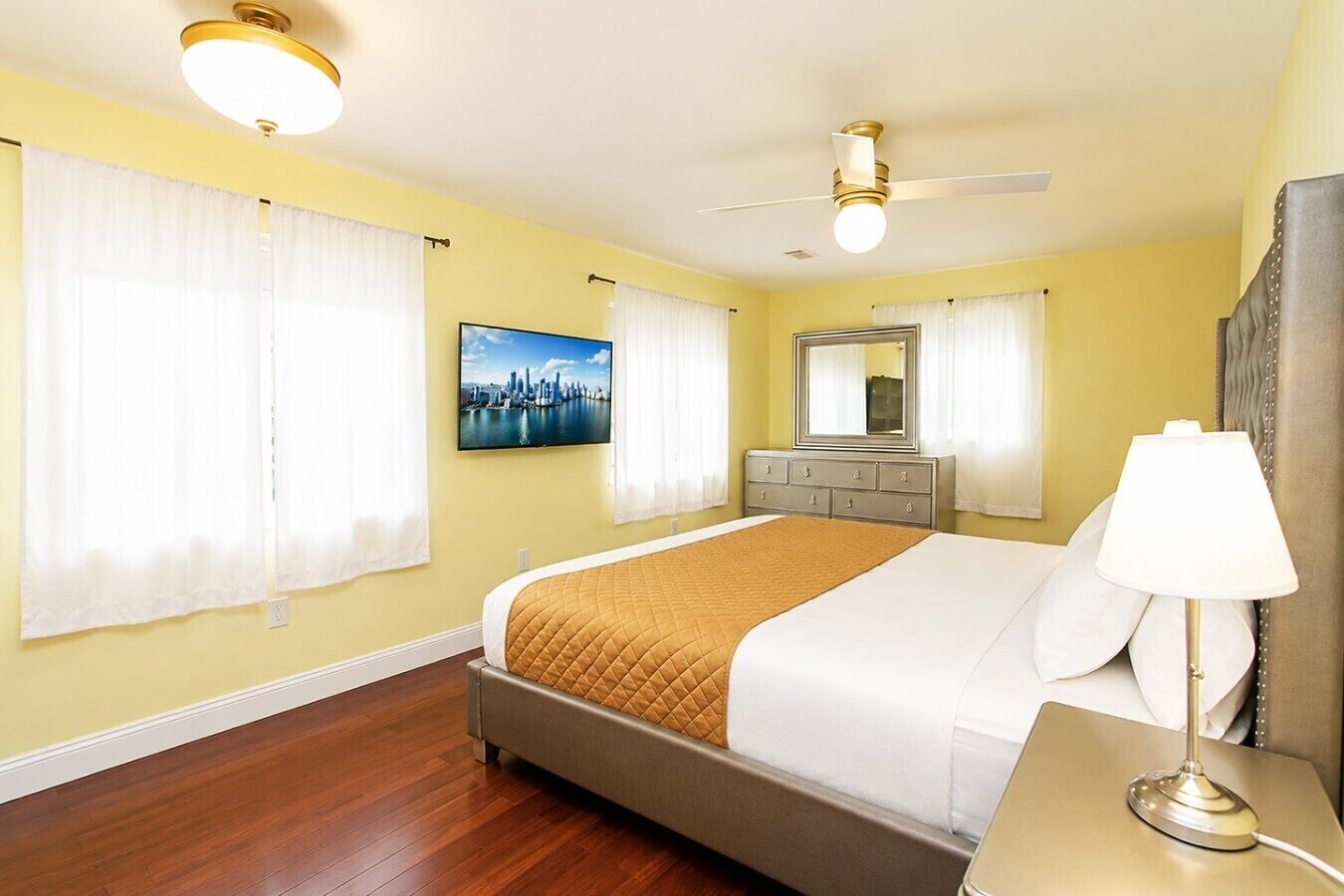A hotel room with a bed, a dresser, a mirror, a television, and a ceiling fan.