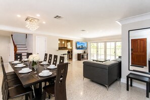 A spacious dining area with a dark wooden table set for six, flanked by dark chairs. A modern chandelier hangs from the ceiling, and a staircase is visible in the background. - First-Class Villa in Hollywood Lakes Heated Pool (Hollywood)