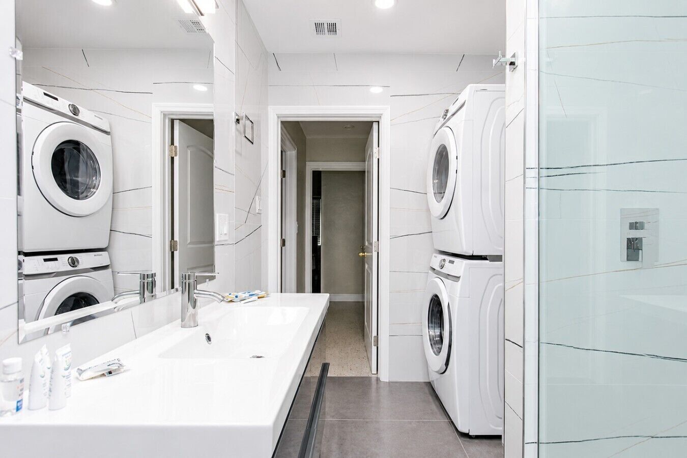 A modern bathroom with a large mirror, a white sink, and two stacked washing machines.