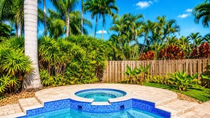 Una piscina con borde de azulejos, rodeada de exuberante follaje y una valla de madera.