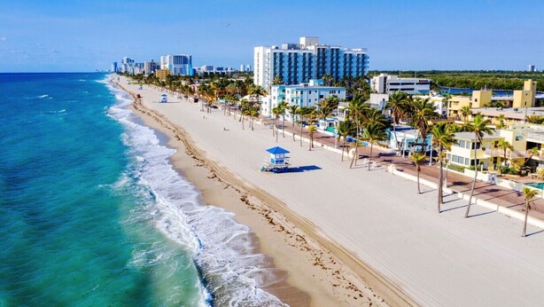 Un hotel frente a la playa con una extensa playa de arena, palmeras y vistas al océano.