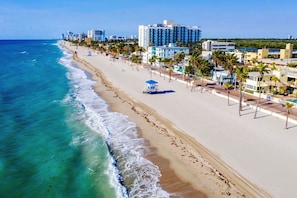 A beachside hotel with a long sandy beach, palm trees, and ocean views.