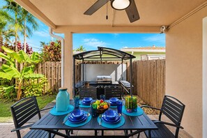 Um pátio externo com mesa posta para refeições, churrasqueira e área de estar coberta.