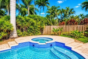 Une piscine dont le bord est revêtu de carrelage, entourée d’une végétation luxuriante et de palmiers.
