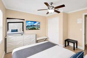 A hotel room with a bed, a desk, a chair, a ceiling fan, a white door, and a cityscape painting on the wall. - Deluxe Home Heated Pool & Jetted Tub near Beach & Casino (Dania Beach)