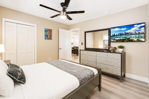A bedroom with a bed, a dresser, a ceiling fan, a large window, and a cityscape painting.