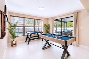 Ein Billardtisch in einem Raum mit großen Fenstern und Blick ins Freie.