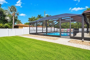 Ein Garten mit Schwimmbad, überdachter Terrasse und weißem Zaun.