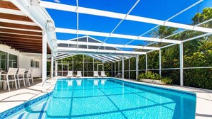 Piscina azul cristalina con techo blanco, rodeada de sillones de descanso blancos y una zona de patio.