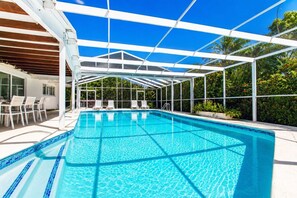 Piscina azul cristalina con techo blanco, rodeada de sillones de descanso blancos y una zona de patio.