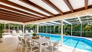 Zona de piscina techada con mesa y sillas, rodeada de follaje.