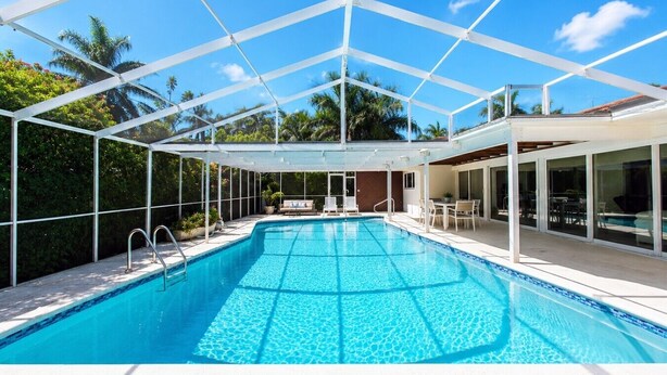 Piscina azul cristalina con techo de estructura blanca, rodeada de vegetación y cielo despejado.