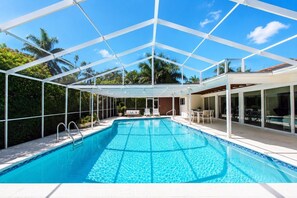 Une piscine d’un bleu éclatant, surmontée d’une structure blanche, entourée de verdure et sous un ciel dégagé.