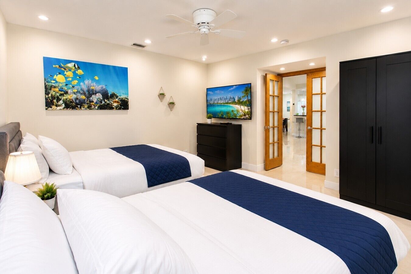 Une chambre d’hôtel avec deux lits, un ventilateur de plafond et des œuvres d’art accrochées aux murs.