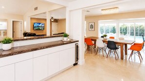 Una cocina moderna con armarios blancos, encimera de granito y comedor con mesa de madera y sillas naranjas.
