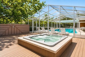 Ein Bereich mit Whirlpool, einer Holzterrasse, Liegestühlen und einem von Glas umgebenen Pool.