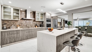 A modern kitchen with a central island, built-in appliances, and a dining area with bar stools. - Spectacular 5BR/5BA Villa in Hollywood Lakes (Hollywood)