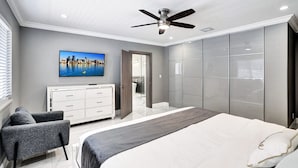 A modern bedroom with a large bed, a ceiling fan, a TV mounted on the wall, and a wardrobe. - Spectacular 5BR/5BA Villa in Hollywood Lakes (Hollywood)