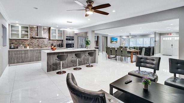 A modern kitchen with a central island, bar stools, and a dining area with a table and chairs. - Spectacular 5BR/5BA Villa in Hollywood Lakes (Hollywood)