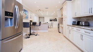 A modern kitchen with a stainless steel refrigerator, white cabinets, and a central island with bar stools. - Ultimate Luxury 5BR Villa near Hollywood Beach (Hollywood)