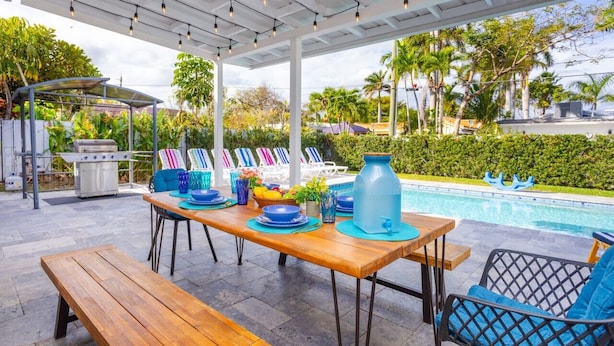 An outdoor dining area with a pool view, covered patio, and lounge chairs. - Ultimate Luxury 5BR Villa near Hollywood Beach (Hollywood)
