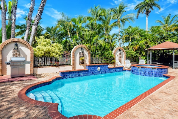 A swimming pool with a tiled edge, a barbecue grill, and a covered seating area.