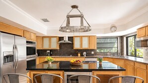 Una cocina moderna con electrodomésticos de acero inoxidable, armarios de madera, una isla central con asientos y un amplio ventanal que proporciona luz natural.