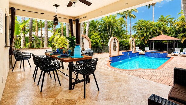 Un espacio al aire libre techado con piscina, sillas y una mesa de comedor.