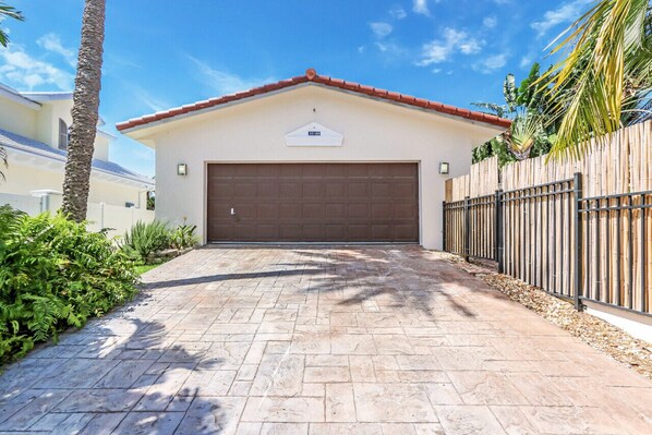 A garage with a brown door, a sign above it, and a paved driveway leading to it.