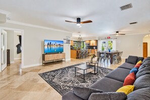 Ein modernes Wohnzimmer mit Fernseher, einer Couch und einem Essbereich mit Stühlen.