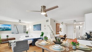A modern living room with a sofa, a dining table set for four, and a kitchen area visible in the background. - Beach Condo - Hollywood Beachfront & Broadwalk (Hollywood)