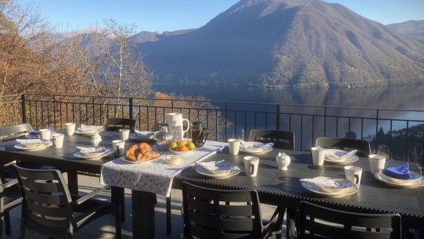 An outdoor dining table set with plates, cups, and a croissant, overlooking a lake and mountains. - Villa Rosa - My Home in Como (Muronico)