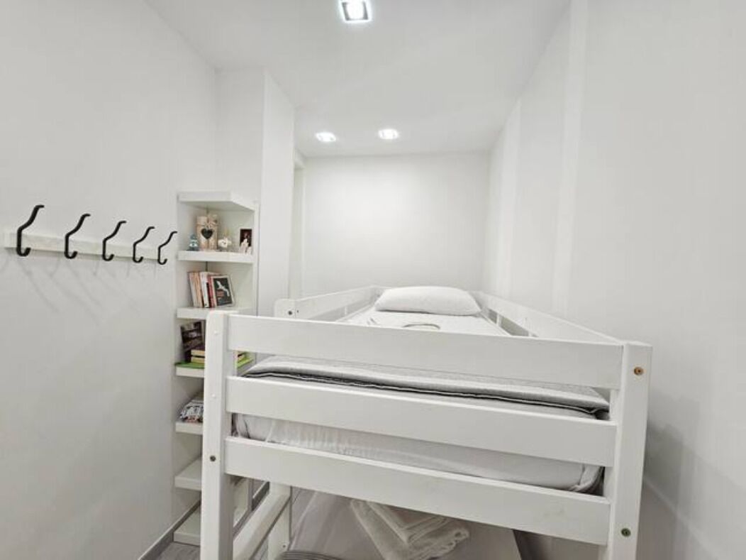 A small, white, single-bed room with a built-in shelf and hooks on the wall.