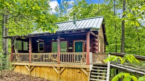 A wooden cabin with a porch, a metal roof, and a wooden deck.