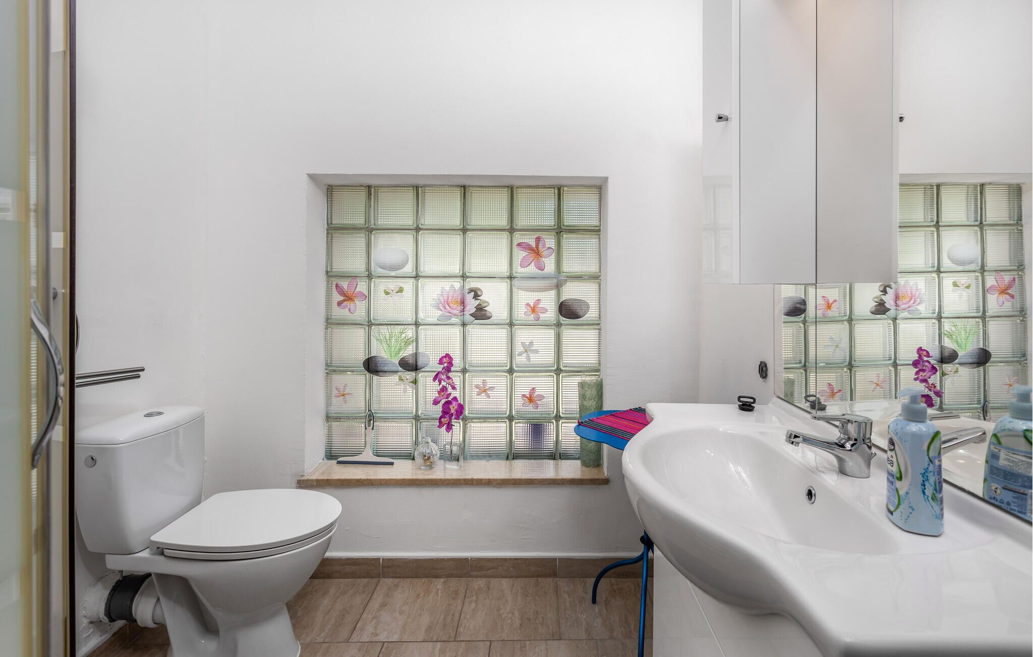 A bathroom with a toilet, a sink, and a window with decorative elements.