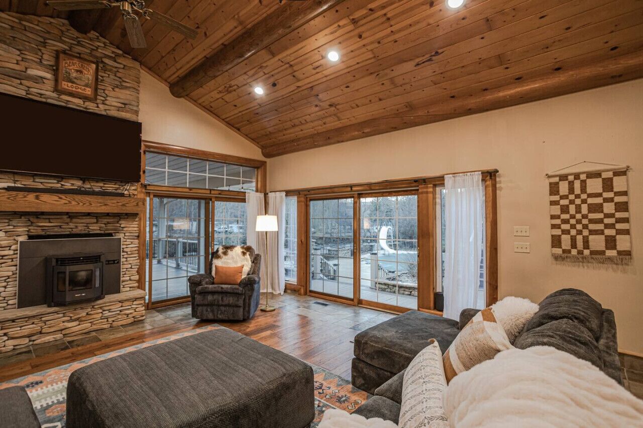 A cozy living room with a stone fireplace, a large window, and a checkered wall hanging.