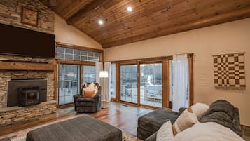A cozy living room with a stone fireplace, a large window, and a checkered wall hanging.