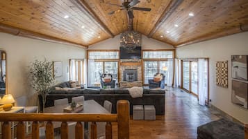 A spacious living area with a large fireplace, wooden ceiling, and a view through large windows.