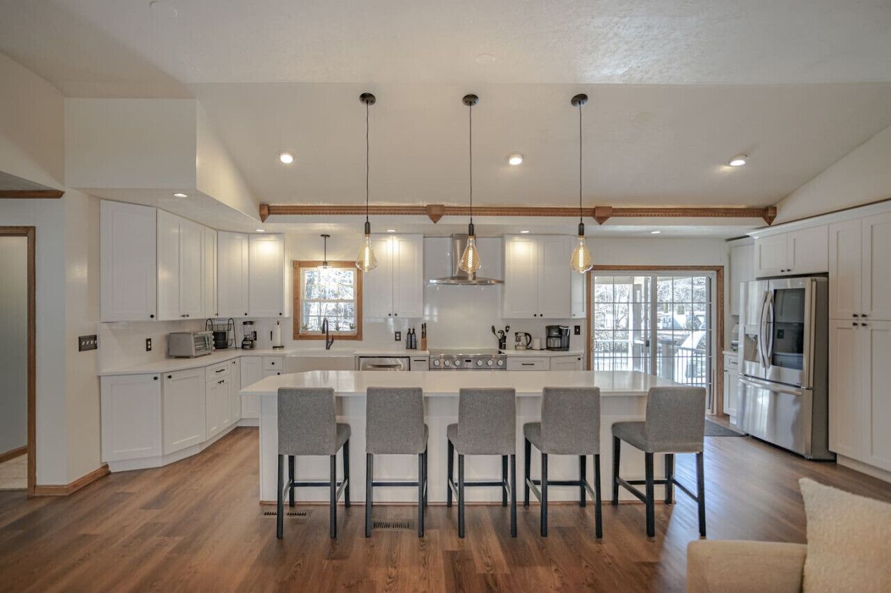 A modern kitchen with white cabinets, a central island with bar stools, and stainless steel appliances.