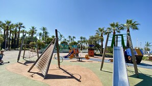 A playground with various play structures, including a slide and swings, surrounded by palm trees and a clear blue sky. - Duplex in Cannes 5 min walk from the beach 5 BR (Cannes)