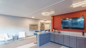 Una cocina moderna con una isla integrada, armarios grises y un televisor de pantalla plana grande montado en una pared de ladrillo rojo.