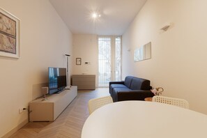 A modern living room with a flat-screen TV, a sofa, a dining table, and a large window.