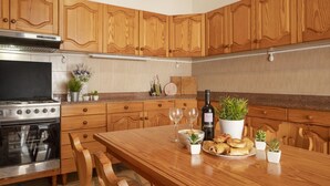 Una cocina con armarios de madera, estufa de acero inoxidable, una mesa de comedor con sillas y una planta en maceta.