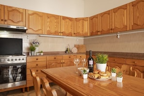 A kitchen with wooden cabinets, a stainless steel stove, a dining table with chairs, and a potted plant.