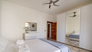 Un dormitorio con cama, cómoda, espejo, ventilador de techo y armario.